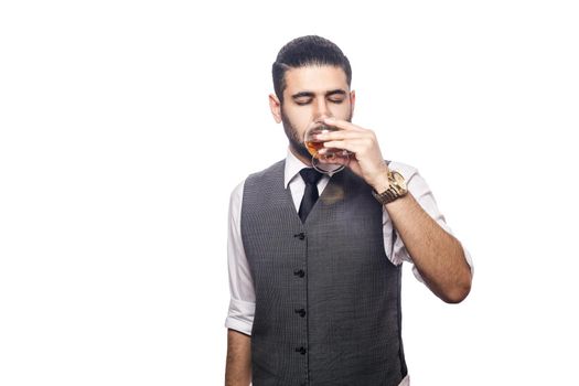 Handsome bearded businessman holding a glass of whiskey. drinking with closed eyes. studio shot, isolated on white background.