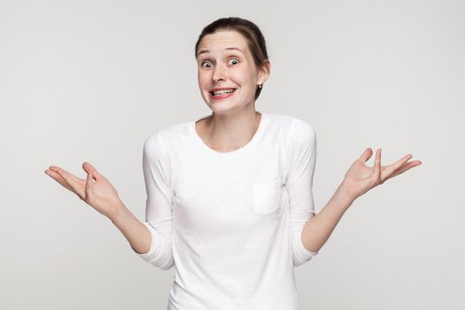 Who knows? Funny woman looking at camera with shocked face. Studio shot,isolated on gray background.