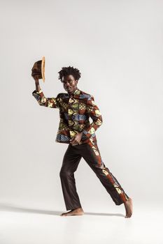 Attractive afro man holding hat and looking at camera. Indoor, isolated on gray background