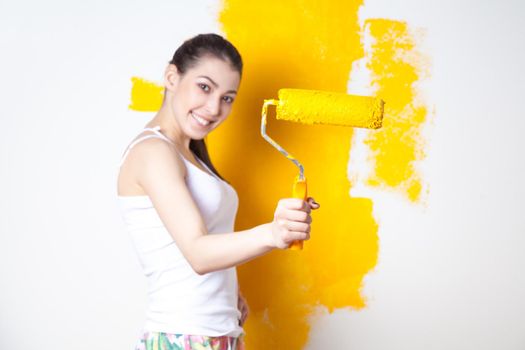 Beautiful young caucasian model in coloured shorts and white shirt and posing holding outrigger in her hands, painting the wall and looking at camera. Studio shot.