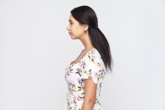 Side view of beautiful young adult woman, standing alone at gray background. Studio shot