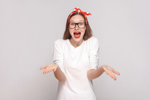 how you did this? it's unbelievable. portrait of beautiful emotional young woman in white t-shirt with freckles, black glasses, red lips and head band. indoor shot, isolated on light gray background.