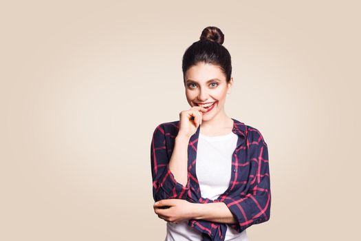 Portrait of beautiful happy toothy smiley girl in casual style looking at camera and toching her lips and teeth with finger and toothy smile. studio shot on beige background.