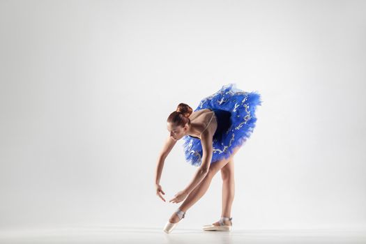 Young beautiful ballerina with bun collected hair wearing blue dress and pointe shoes dancing gracefully isolated on white background. indoor, studio shot.