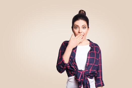 Portrait of young desperate woman in casual style amd bun hairstyle looking surprised, with mouth wide open and hands. Female in despair and shock