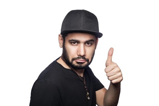 Portrait of young man with black t-shirt and cap looking at camera with thumbs up. studio shot, isolated on white background.
