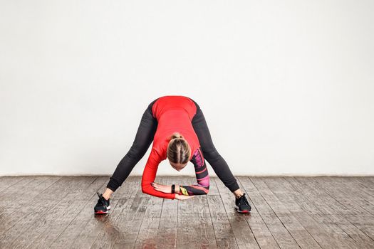 Athletic young slim woman in tight sportswear bending leaning down, stretching muscles for flexibility, warming up before training in gym home. Health care, sports activity. indoor studio shot