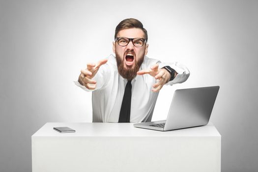 Portrait of aggressive angry young businessman in white shirt and black tie are blaming you in office and having bad mood, screaming and want to strangle you. Indoor, studio shot, gray background