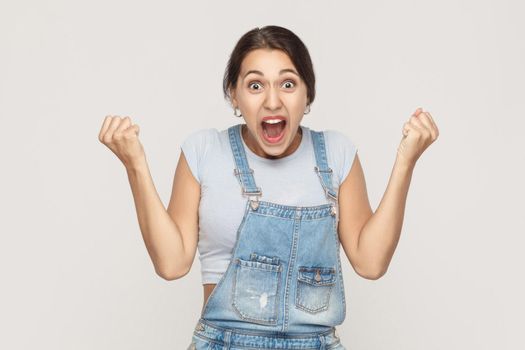 Happiness woman in denim overalls rejoicing for his success. Isolated on gray background. Indoor, studio shot