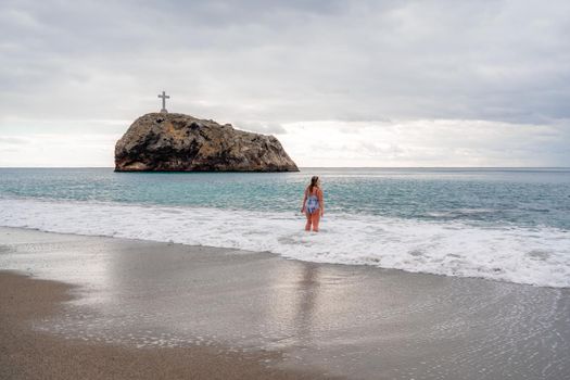 A plump woman in a bathing suit enters the water during the surf. Alone on the beach, Gray sky in the clouds, swimming in winter