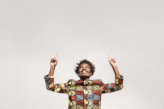 Happiness african man pointing finger up at copy space. Indoor, isolated on gray background