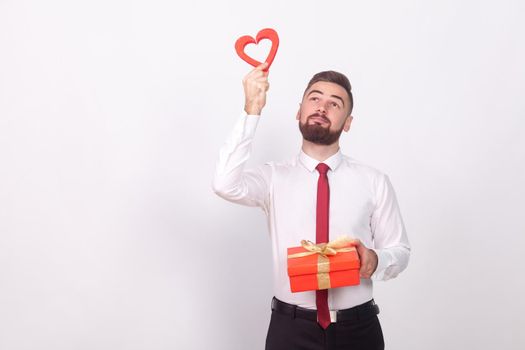 Young man holding gift box and dreaming of love. Indoor, studio shot, isolated on gray background