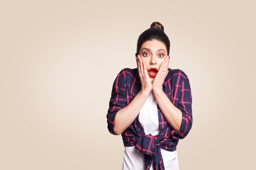 Portrait of young desperate redhead woman in casual style looking panic, holding her head with both hands, with mouth wide open. Female in despair and shock.