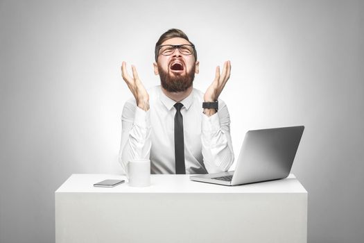 No way! Portrait of emotional scared young manager in white shirt and black tie are sitting in office and screaming and crying cause made big mistake with raised arms and stressed face. Studio shot