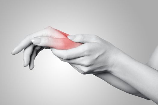 Closeup view of a young woman with pain on hand on gray background. Black and white photo with red dot.