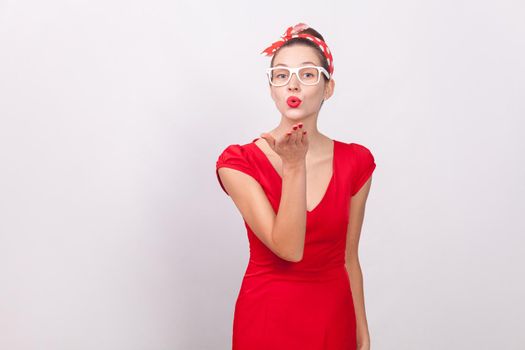 Cute beautiful woman send air kiss with love. Indoor, studio shot, isolated on gray background