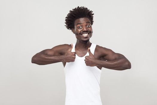 Funny afro man with mustache, looking at camera, smiling, thumbs up. Studio shot. Gray background