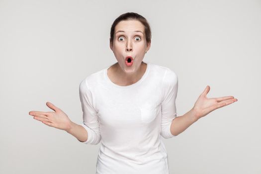 Surprised young woman looking at camera with open mouth and big eyes. Studio shot, gray background