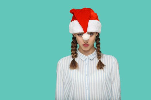 New year concept. funny beautiful girl in striped light blue shirt in red christmas cap and pigtail hair standing and looking at camera and kissing. indoor, studio shot isolated on green background.