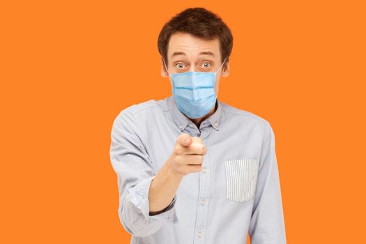 You? Portrait of shocked or surprised young worker man with surgical medical mask standing pointing and looking at camera with amazed face and asking. indoor studio shot isolated on orange background.