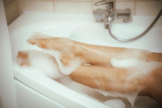 Women's feet in bath foam. View from above. Enjoy and relax in a spa hotel.