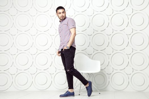 Young bearded fashion model in casual style is posing near white circle wall background. studio shot. posing and looking away with hand on packet.