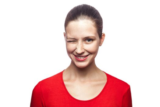 Portrait of funny positive winking woman in red t-shirt with freckles. looking at camera with toothy smile, studio shot. isolated on white background.