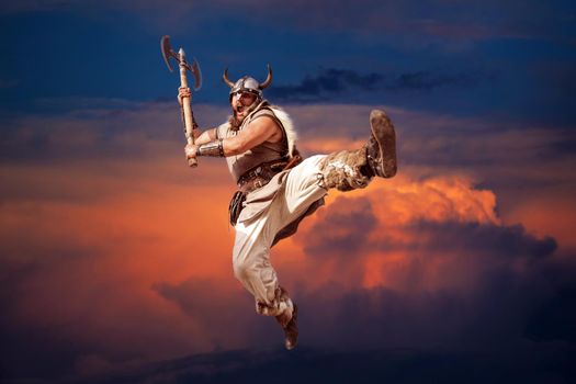 crazy strong viking with traditional costume attacking from sky in the sunset background. looking at camera with angry eyes.