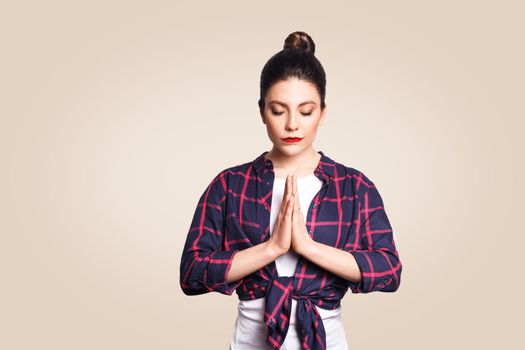 Young brunete woman practising yoga, holding hands in namaste and keeping her eyes closed. Caucasian girl meditating indoors, praying for peace and love, having calm and peaceful facial expression.