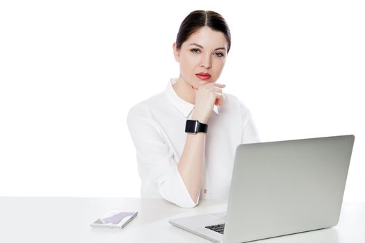 Portrait of serious successful brunette businesswoman in white shirt sitting with laptop, touhing her chin and looking at camera with thoughtful face. indoor studio shot, isolated in white background.