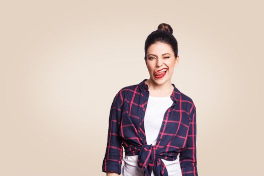 Portrait of beautiful happy girl in casual style looking at camera with funny face and tongue out and wink. studio shot on beige background.