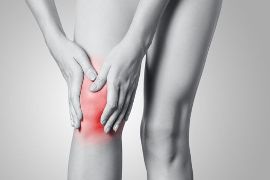 Closeup view of a young woman with knee pain on gray background. Black and white photo with red dot.