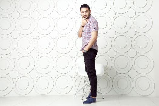 Young bearded fashion model in casual style is posing near white circle wall background. studio shot. looking at camera with smile.