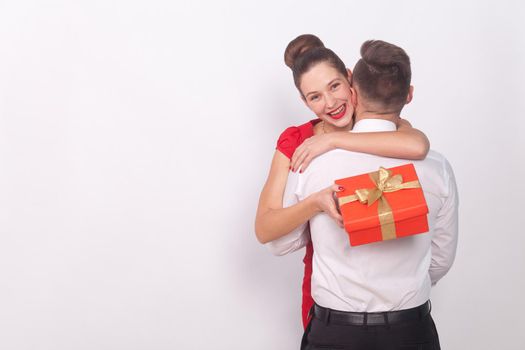 Happy girl has received a gift, toothy smile, embrace her man. Indoor, studio shot, isolated on gray background