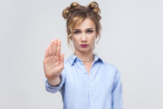 Blonde woman with bad attitude making stop gesture with her palm outward, saying no, expressing denial or restriction. Studio shot