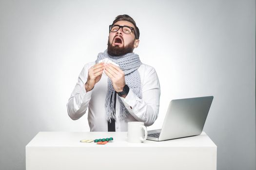 Portrait of sick scribble young boss in white shirt, scarf and black tie are sitting in office and need to finish important report, have grippe virus. Studio shot, isolated, gray background, indoor