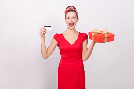 Shocked beautiful wonder woman, holding credit card, gift box.. Indoor, studio shot, isolated on gray background