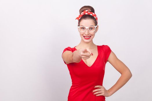 Happiness woman in red dress pointing finger an toothy smile . Indoor, studio shot, isolated on gray background