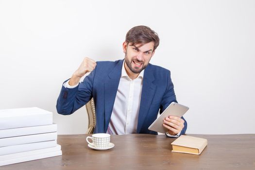 Technology, people and business concept - handsome man with beard and brown hair and blue suit and tablet pc computer and some books sitting in the office angry and unhappy. .Isolated on white background. .