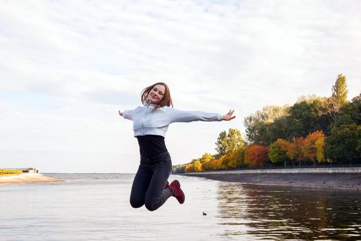 Beautiful girl jumping on the park road near lake. Happiness and cute young adult model. Outdoor shot