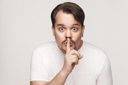 Shh sign. Man with big eyes looking at camera with silent sign. Studio shot, on gray background.