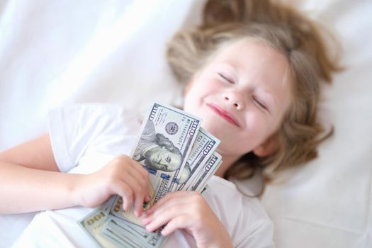 Little happy baby girl sleeps with cash dollars. Childish dreams and wealth concept