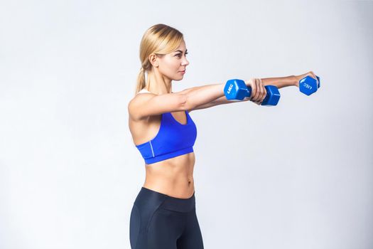 Profile view of blonde woman, showing two blue dumbbells. Isolated on gray background, studio shot