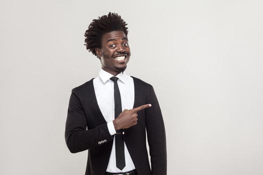 Businessman pointing finger at copy space and tothy smiling . Studio shot, gray background