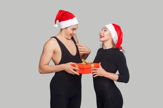 Surprised man holding gift box and looking at her woman and asking is it realy for me?. Studio shot, indoor isolated on gray background.