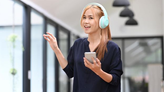 Pretty asian woman wearing headphones enjoy favorite song while spending free time at home. Mood, hobby, modern wireless technology concept.