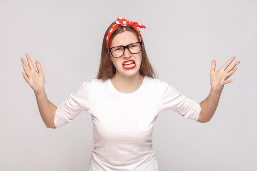 what do you want? portrait of unsatisfied angry emotional young woman in white t-shirt with freckles, black glasses, red lips and head band. indoor studio shot, isolated on light gray background.