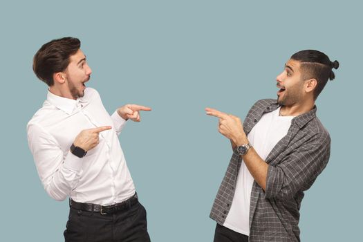 Is that you? profile side view of two handsome funny wondered bearded friends standing and pointing to each other with amazed face and asking. indoor studio shot, isolated on light blue background.