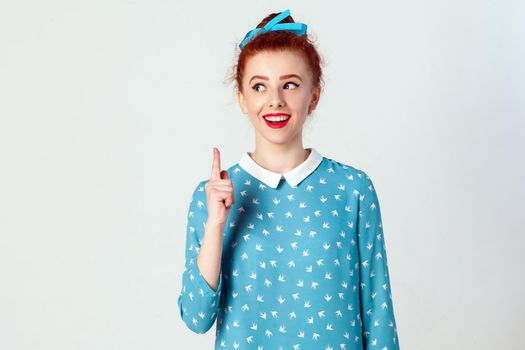 The beautiful redhead girl got the idea and she raised her finger up. Isolated studio shot on gray background