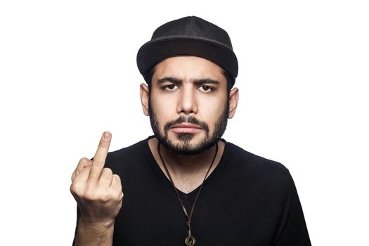 Portrait of young angry man with black t-shirt and cap looking at camera and showing middle finger. studio shot, isolated on white background.